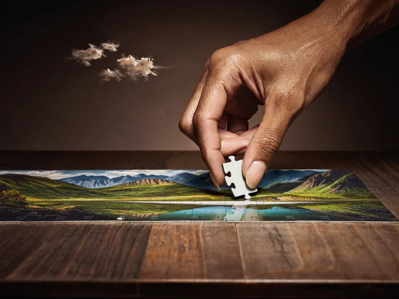 Puzzle panoramic lung desfășurat pe masă cu o mână care așază o piesă